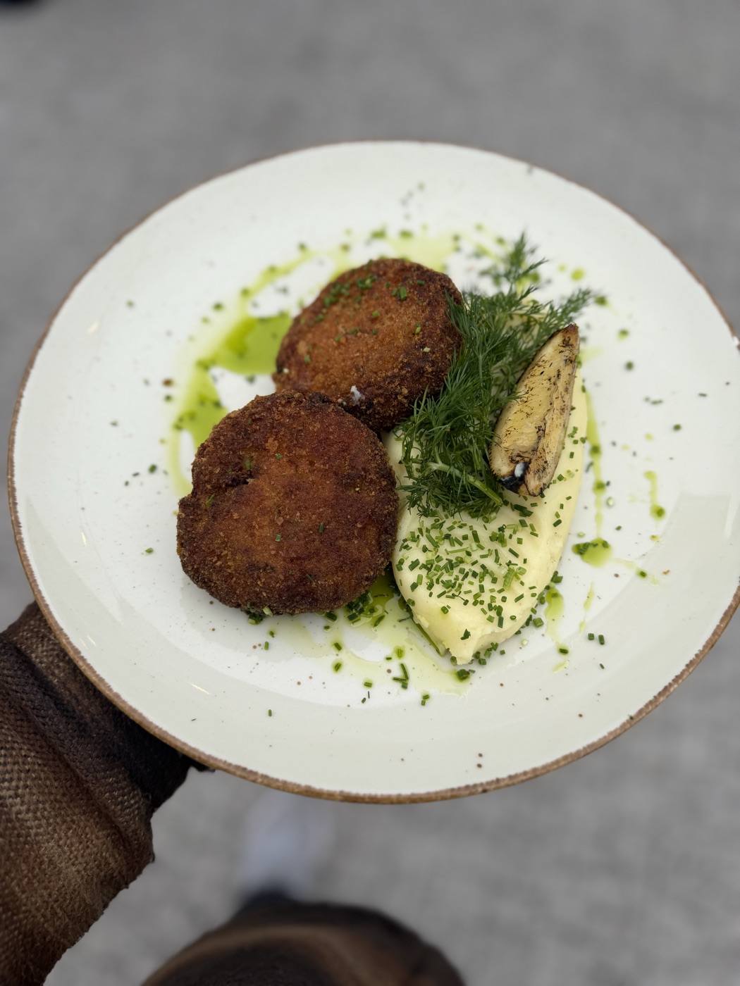 Kotlet mielony rybny — dwa panierowane kotlety podane z puree ziemniaczanym, koperkiem, zieloną oliwą i pieczoną pieczarką