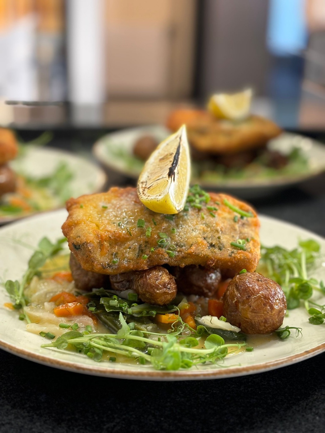 Schabowy z dorsza — panierowany filet z dorsza ułożony na ziemniakach w mundurkach, marchewce, fasolce i zasmażanej kapuście, z grillowaną cytryną i mikrozieleniną