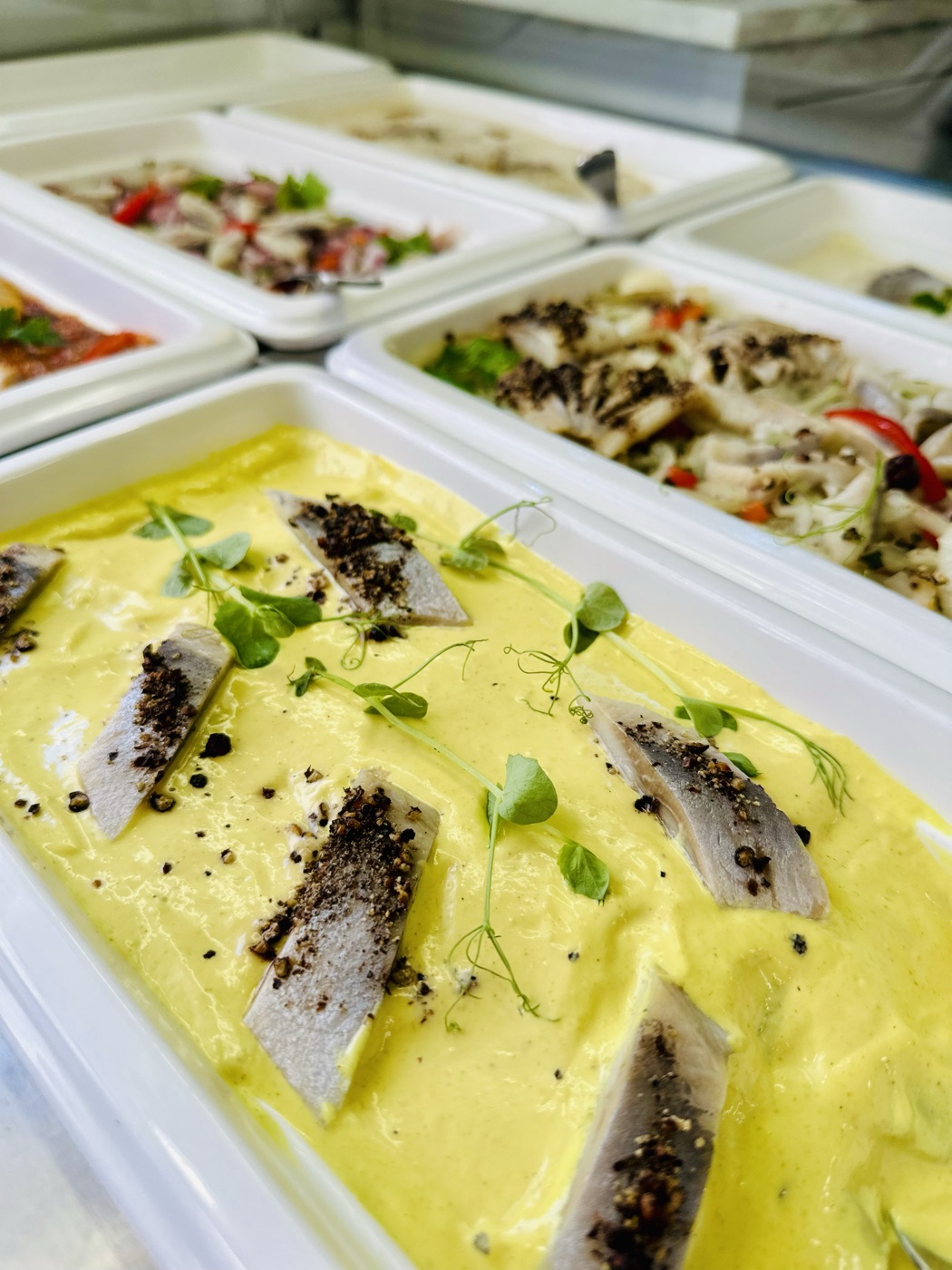 Wariacje śledziowe na wagę — witryna z kilkoma rodzajami śledzia: w żółtym sosie z kiełkami, z jarzynami, z papryką i cebulą